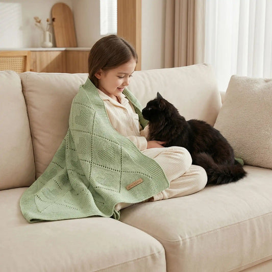 petite fille avec une couverture bébé tricotée vert sauge sur les épaules qui caresse un chat noir à long poils