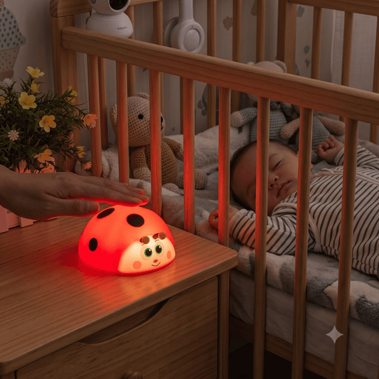 veilleuse bébé coccinelle à lumière rouge posée sur une table de chevet avec un bébé qui dort profondément dans son lit à barreaux