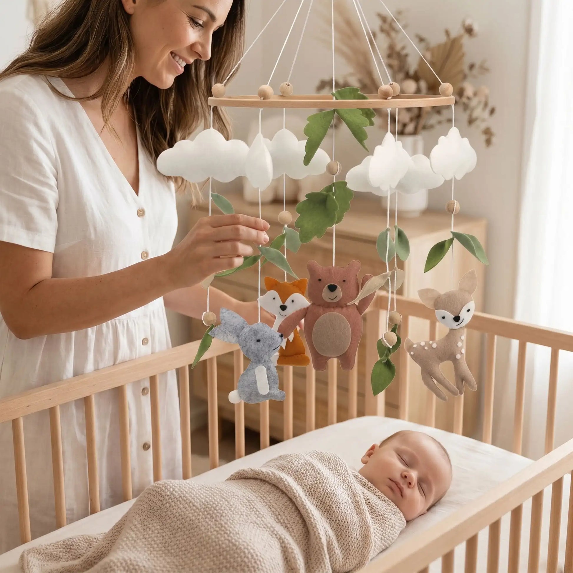 Mobile bébé en bois et feutre suspendu au-dessus d'un berceau dans une chambre de nouveau-né au style naturel