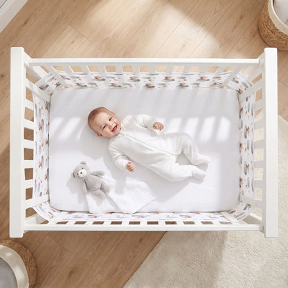 vue aérienne d'un bébé qui sourit dans son lit couché sur le dos dans son lit à barreaux avec un tour de lit bébé filet anti étouffement ourson
