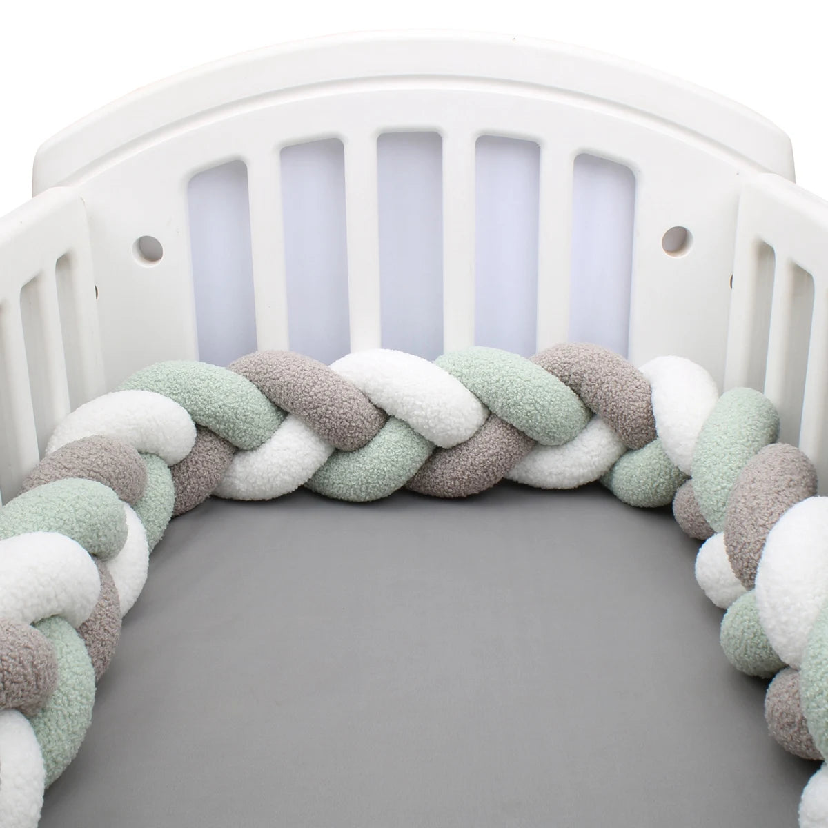 contour de lit tressé 3 brins vert sauge 3 couleurs installé autour des barreaux d'un lit bébé