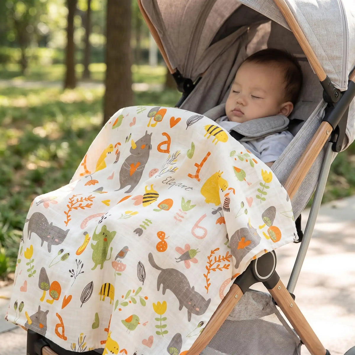 Nouveau-né endormi paisiblement dans sa poussette, recouvert par une douce couverture en gaze de coton aux couleurs automnales avec motifs renard et chat