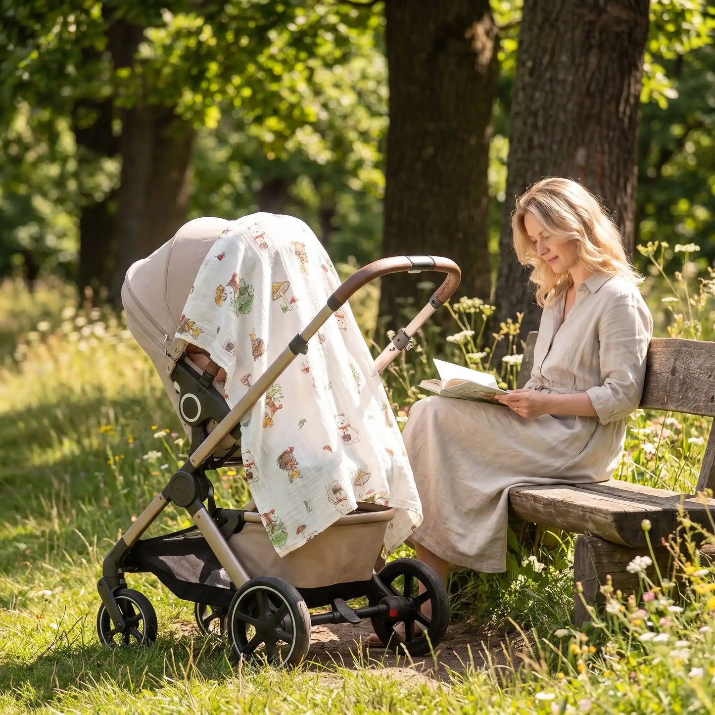 Maman assise sur un banc en extérieur à côté d'une poussette, protégée du vent par une couverture bébé en gaze de coton aux motifs renard, écureuil et champignons