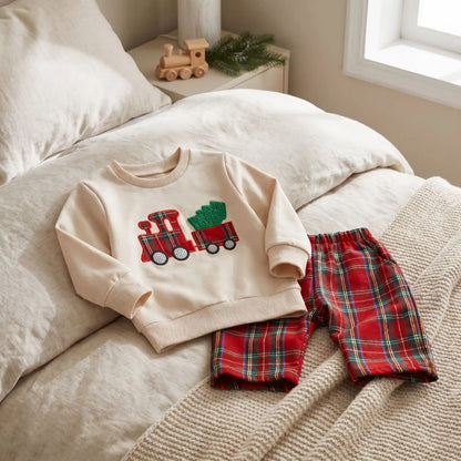 ensemble noel bébé garcon posé sur un lit d'enfant avec un train tirant un sapin et un pantalon à carreaux rouge 