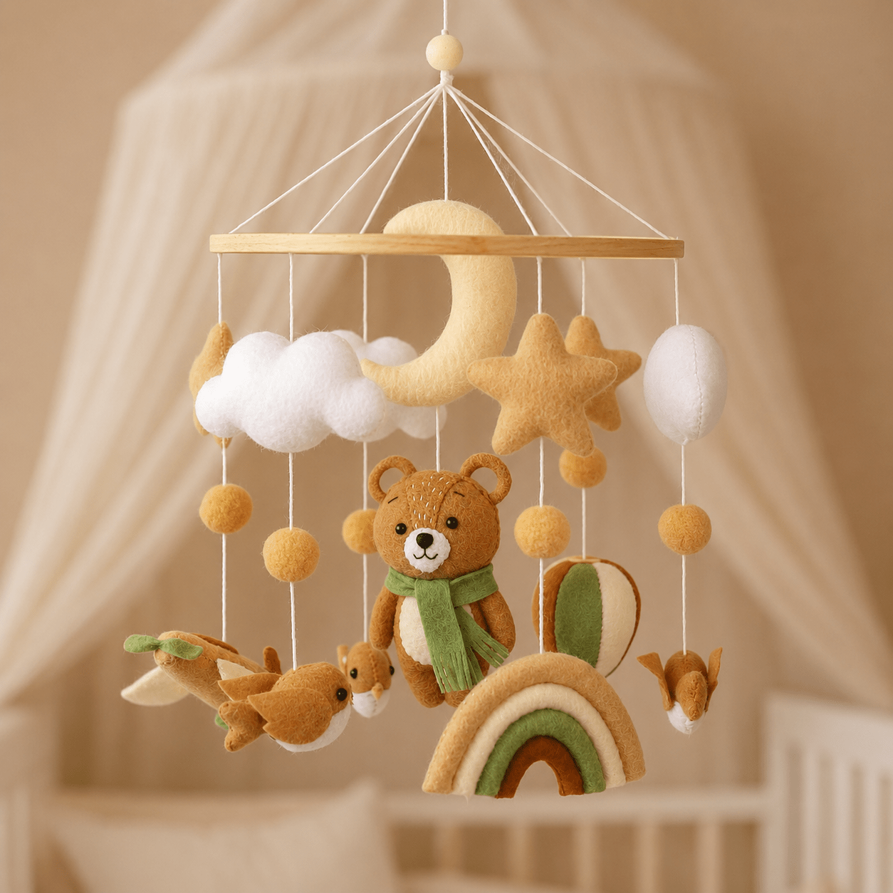 Mobile bébé artisanal thème automne  avec un ours en feutrine au foulard vert, un arc-en-ciel, des oiseaux, une lune et une étoile en tissu au-dessus d'un berceau.