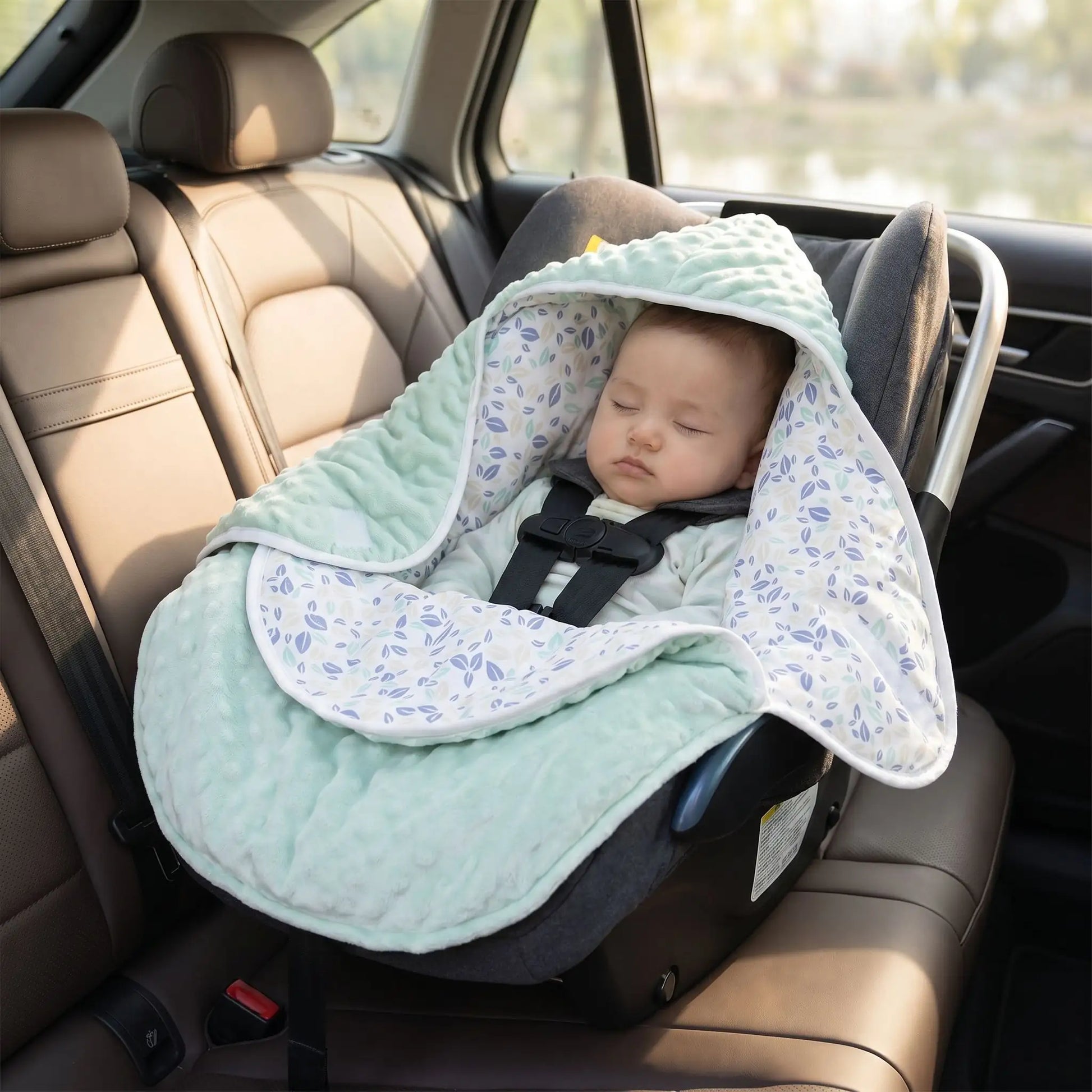 bébé dans un siège auto placé dans une voiture enveloppé dans un nid d'ange cosy vert réversible
