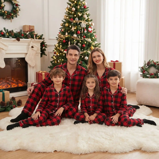 Parents et trois enfants posant en pyjamas de Noël assortis boutonnés à carreaux rouges et noirs sur un tapis blanc devant la cheminée.