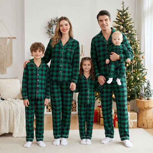 Parents et trois enfants debout en pyjamas de Noël famille assortis boutonnés à carreaux vert et noir avec liseré blanc devant le sapin de Noël.