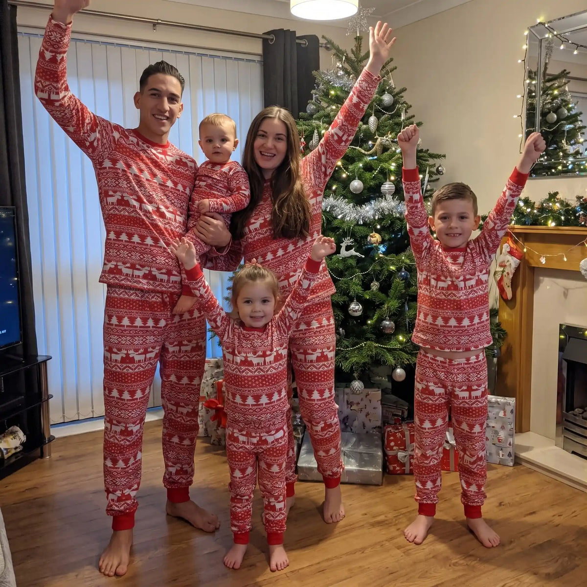 dans un salon décoré sur le thème de noël, une famille entière en pyjama de noël pour toute la famille rouge et blanc aux motifs sapin et rennes