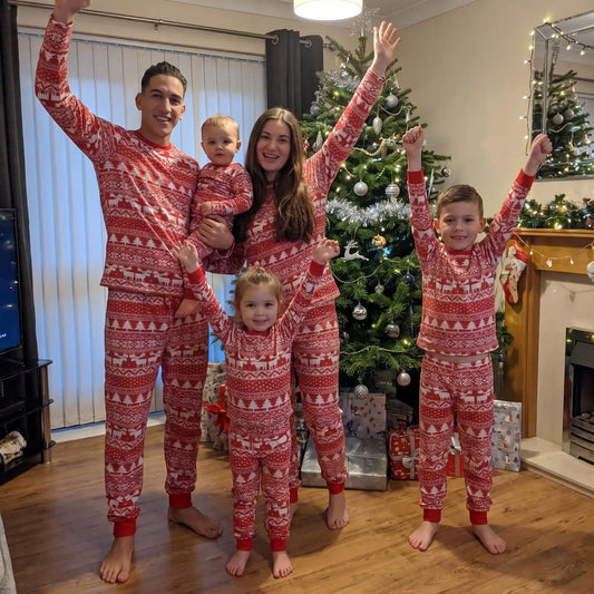 dans un salon décoré sur le thème de noël, une famille entière en pyjama de noël pour toute la famille rouge et blanc aux motifs sapin et rennes