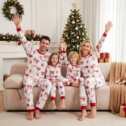 Famille souriante sur un canapé portant des pyjamas de Noël assortis blancs à motifs Père Noël et rennes devant le sapin.