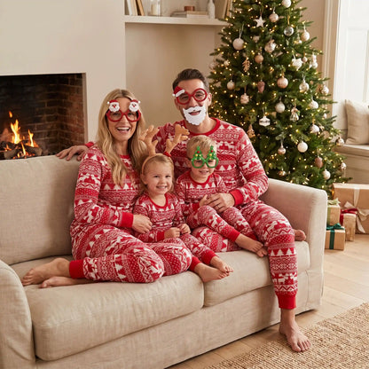 un couple et leur deux enfants assis sur un canapé habillés chacun d'un pyjama noel famille rouge et blanc traditionnel avec motifs rennes