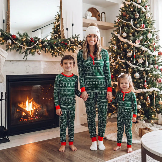 une maman souriante tient les mains de chaque côté de ses enfants tous habillées en pyjama de noel assorti famille sapin vert 