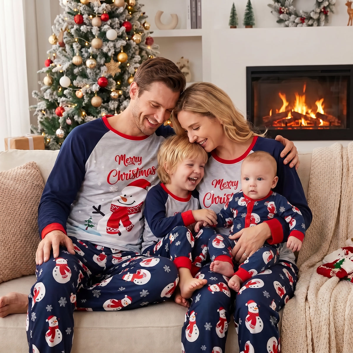 un couple avec leur enfant de 4 ans et leur bébé assis sur un canapé tous habillés avec un pyjama de noel parents et bébé bonhomme de neige assorti