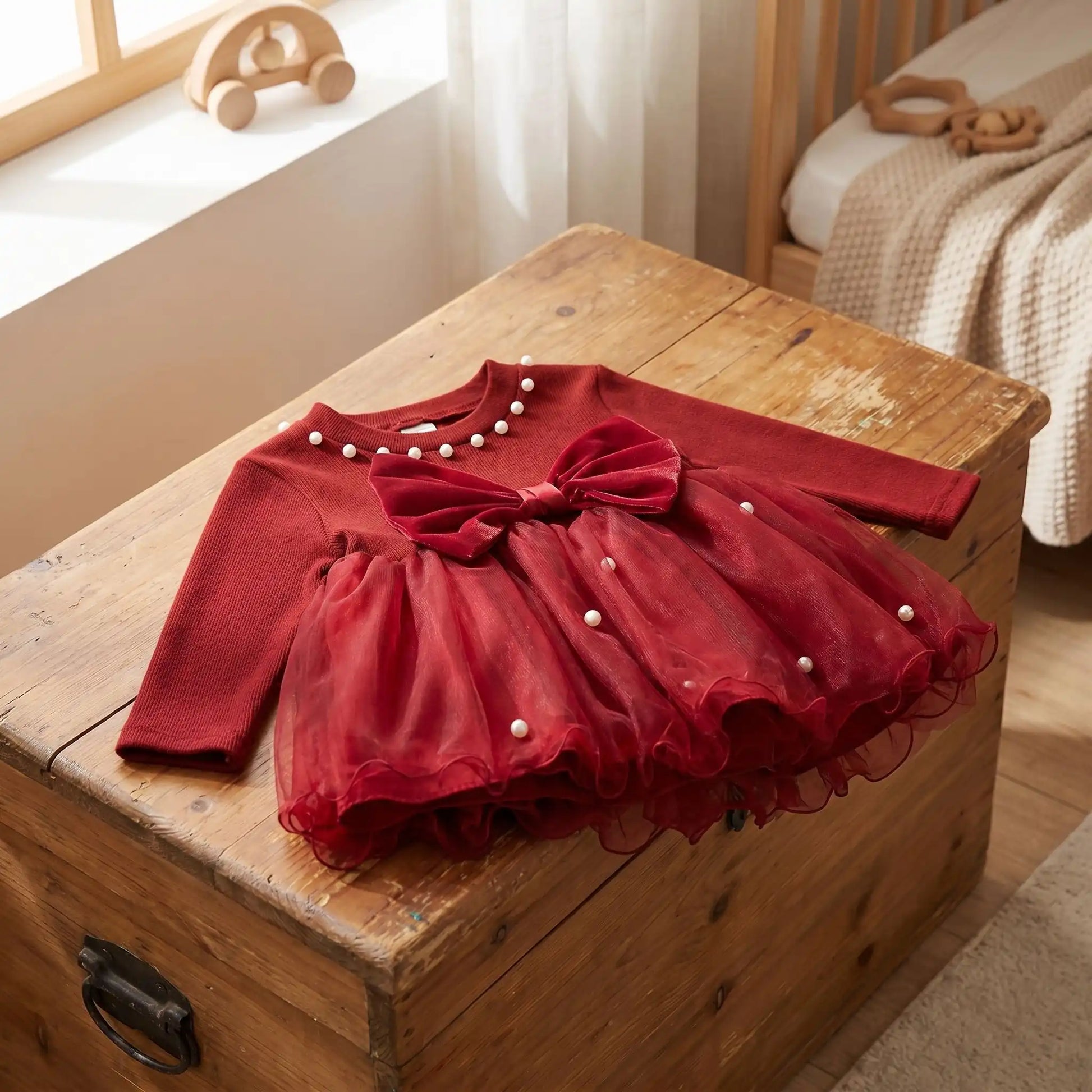 zoom sur une petite robe de noel pour bébé fille de 5 mois à 3 ans posée sur un coffre à jouets en bois