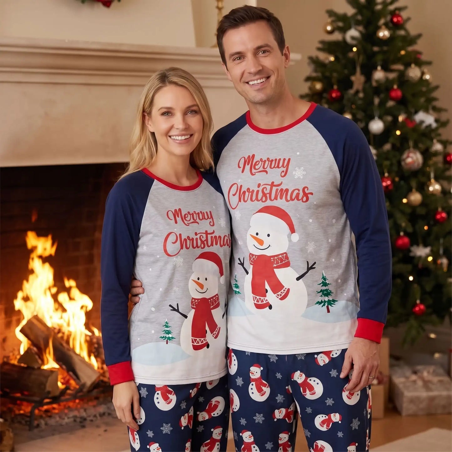 couple souriant devant une cheminée allumée qui porte une tenue pour noël 2026 avec en motif un bonhomme de neige