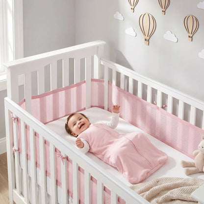 bébé fille dans sa gigoteuse qui sourit dans son lit à barreaux blanc avec un tour de lit respirant rose fixé par des liens tout autour du lit