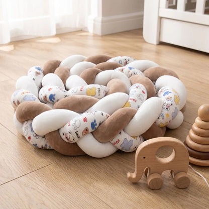 Tour de lit bébé tressé marron et blanc enroulé en escargot sur un plancher en bois dans une chambre d'enfant