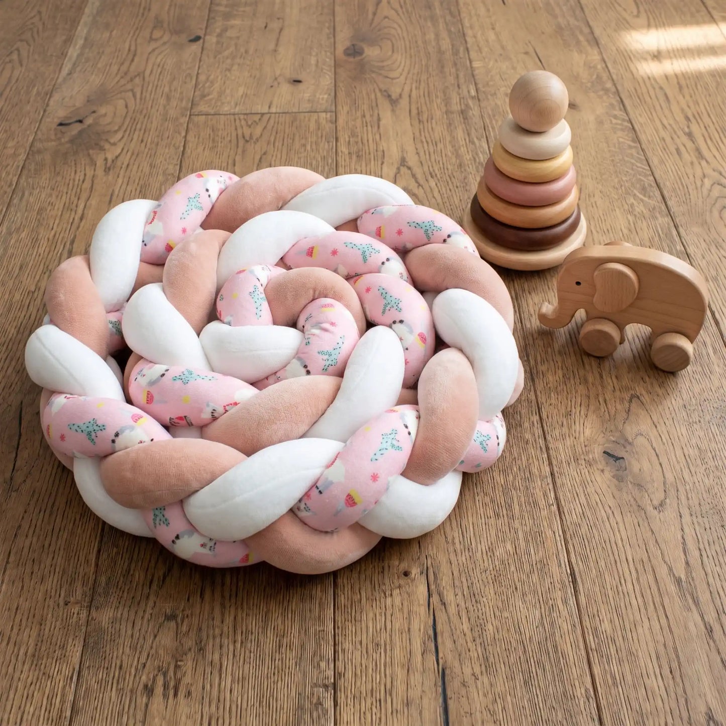 Tresse de lit bébé 3 brins rose délicat enroulée sur elle-même posée sur le parquet d'une chambre d'enfant