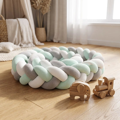 tour de lit tressé vert sauge entouré sur lui même posé sur un plancher en bois avec des jouets en bois à côté