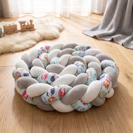 Tresse de lit bébé 3 brins grise et blanche enroulée sur elle-même posée sur un plancher de chambre