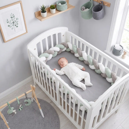 Vue aérienne d'un bébé couché dans son lit à barreaux, protégé par une tresse de lit bébé vert sauge de 4 mètres qui fait tout le tour de l'intérieur du berceau.