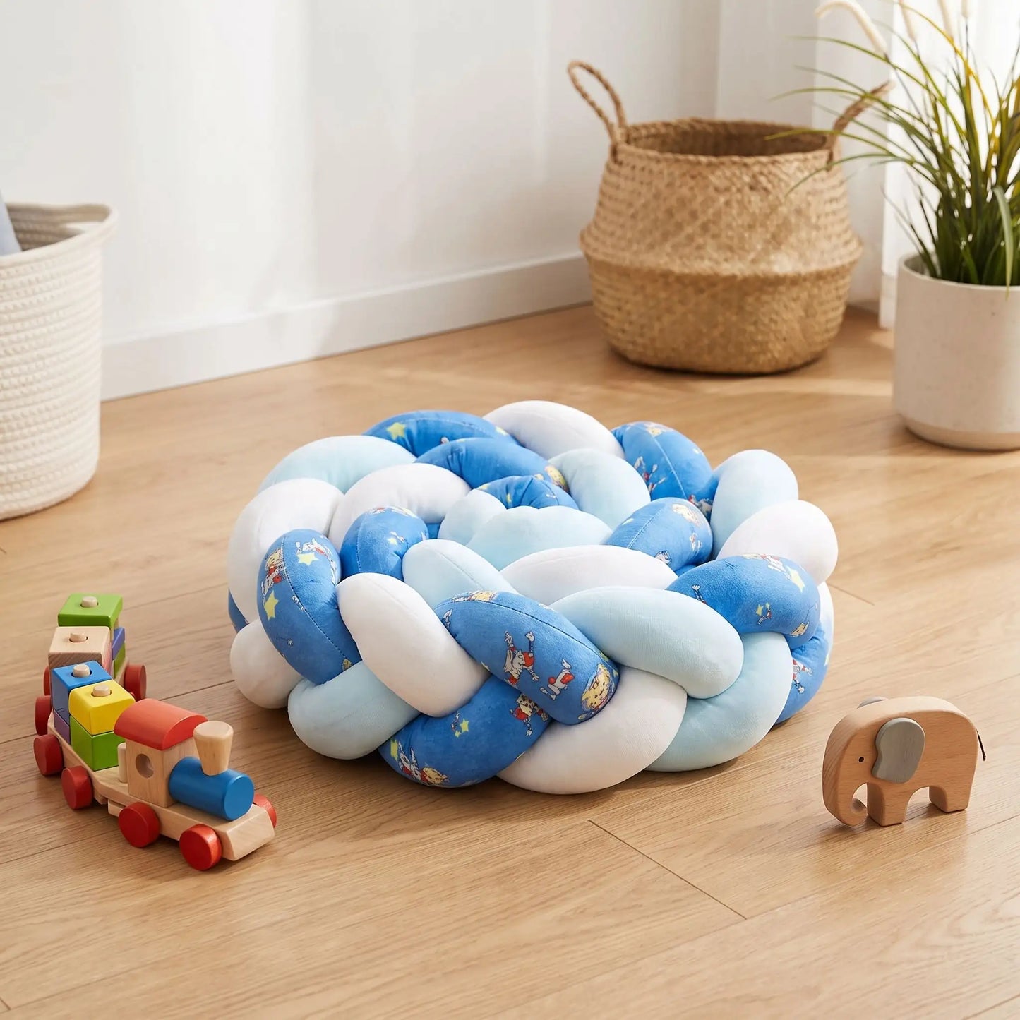 Tresse de lit 3 brins bleue et blanche enroulée sur elle-même, posée sur le parquet d'une chambre de bébé