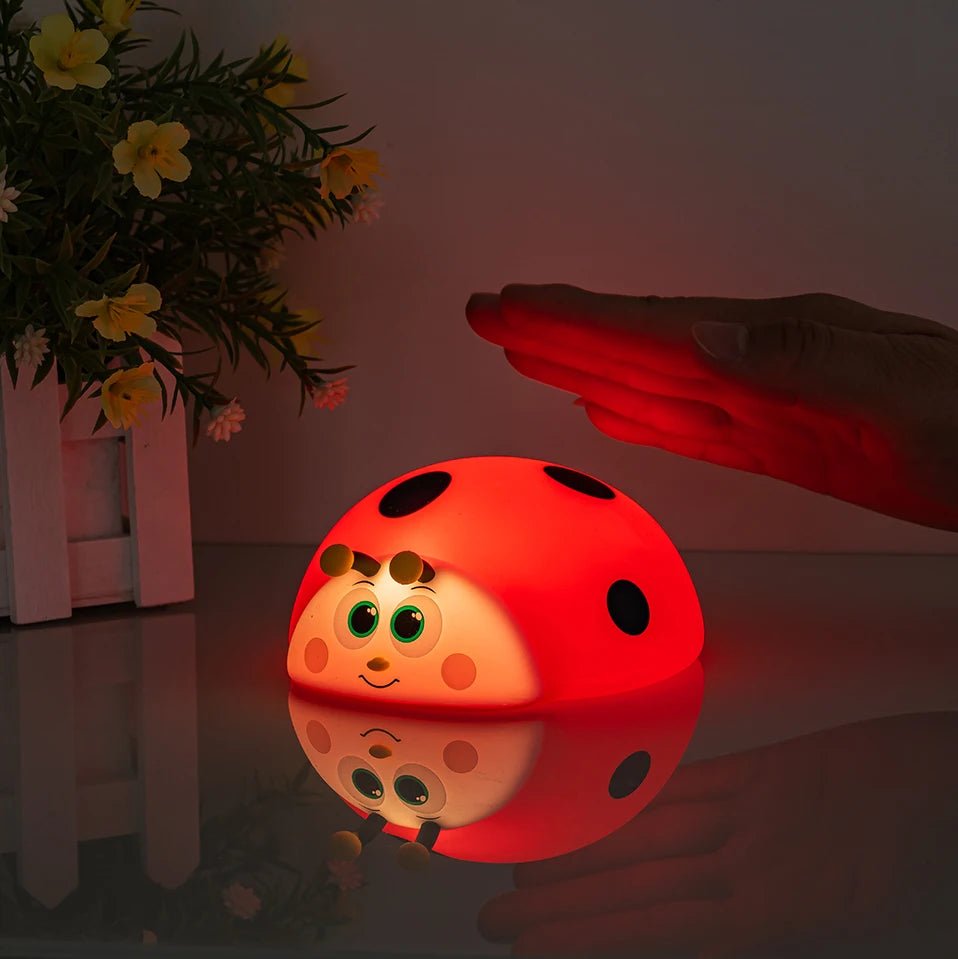 veilleuse coccinelle pour bébé posée sur une table qui diffuse de la lumière rouge douce et apaisante avec une main qui est au dessus de la veilleuse  pour changer de mode