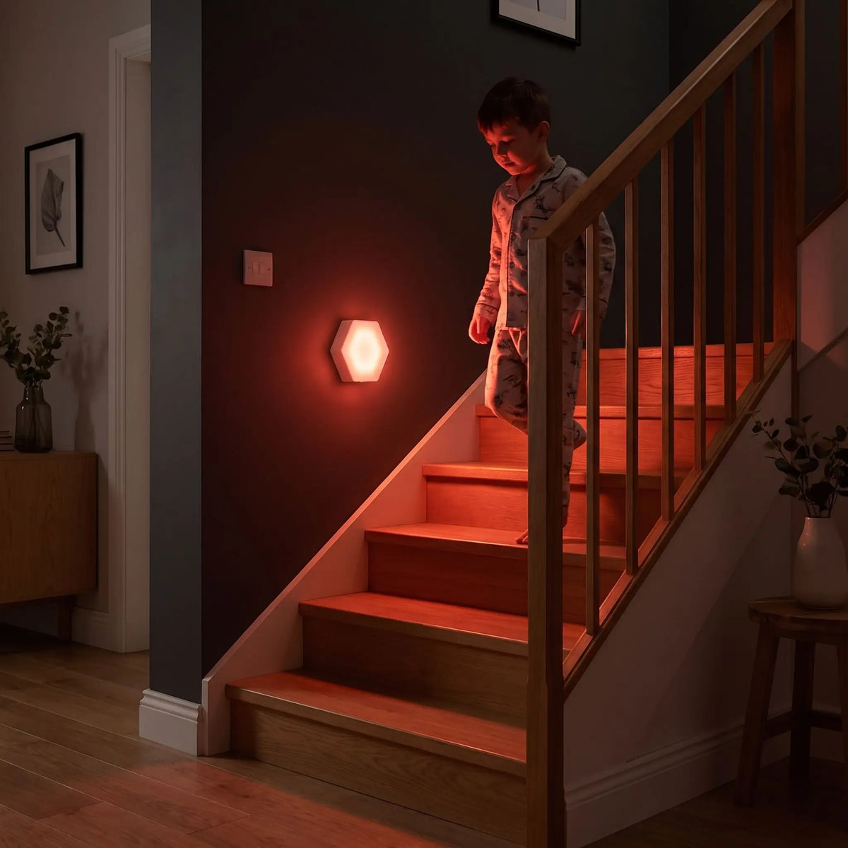 Veilleuse bébé lumière rouge à détecteur de mouvement fixée au mur d'un escalier pour guider un enfant la nuit et éviter les chutes.
