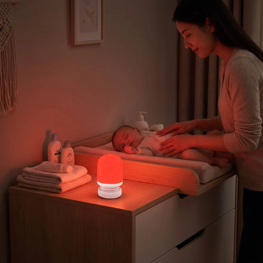maman qui change son bébé endormi dans la nuit avec une veilleuse rouge sommeil qui diffuse une lumière apaisante posée sur la table à langer